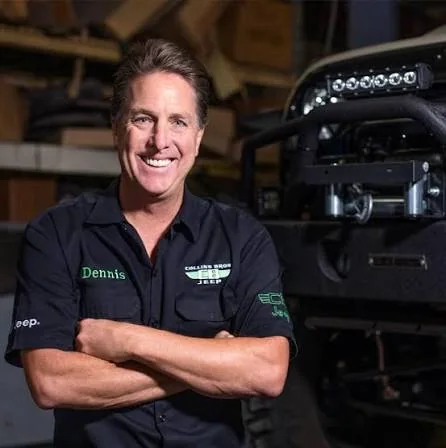 Dennis Collins, arms folded, in front of a Jeep in his shop.